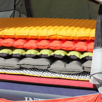 This best sleeping pad reviews photo shows several air mattresses and sleeping pads for camping and backpacking stacked up in a tent.