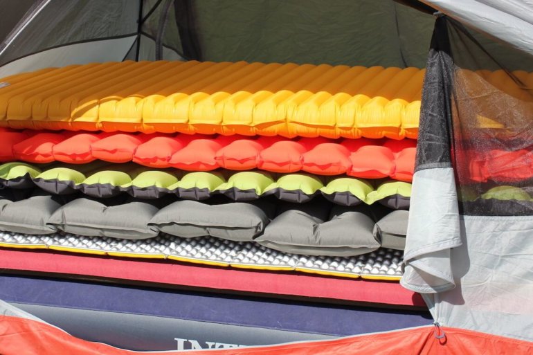 This best sleeping pad reviews photo shows several air mattresses and sleeping pads for camping and backpacking stacked up in a tent.