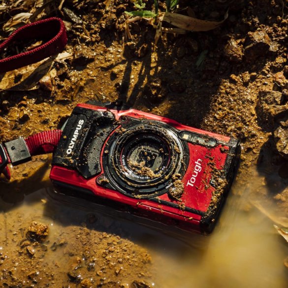 This image shows the Olympus Tough TG-5 waterproof camera on the ground in mud.