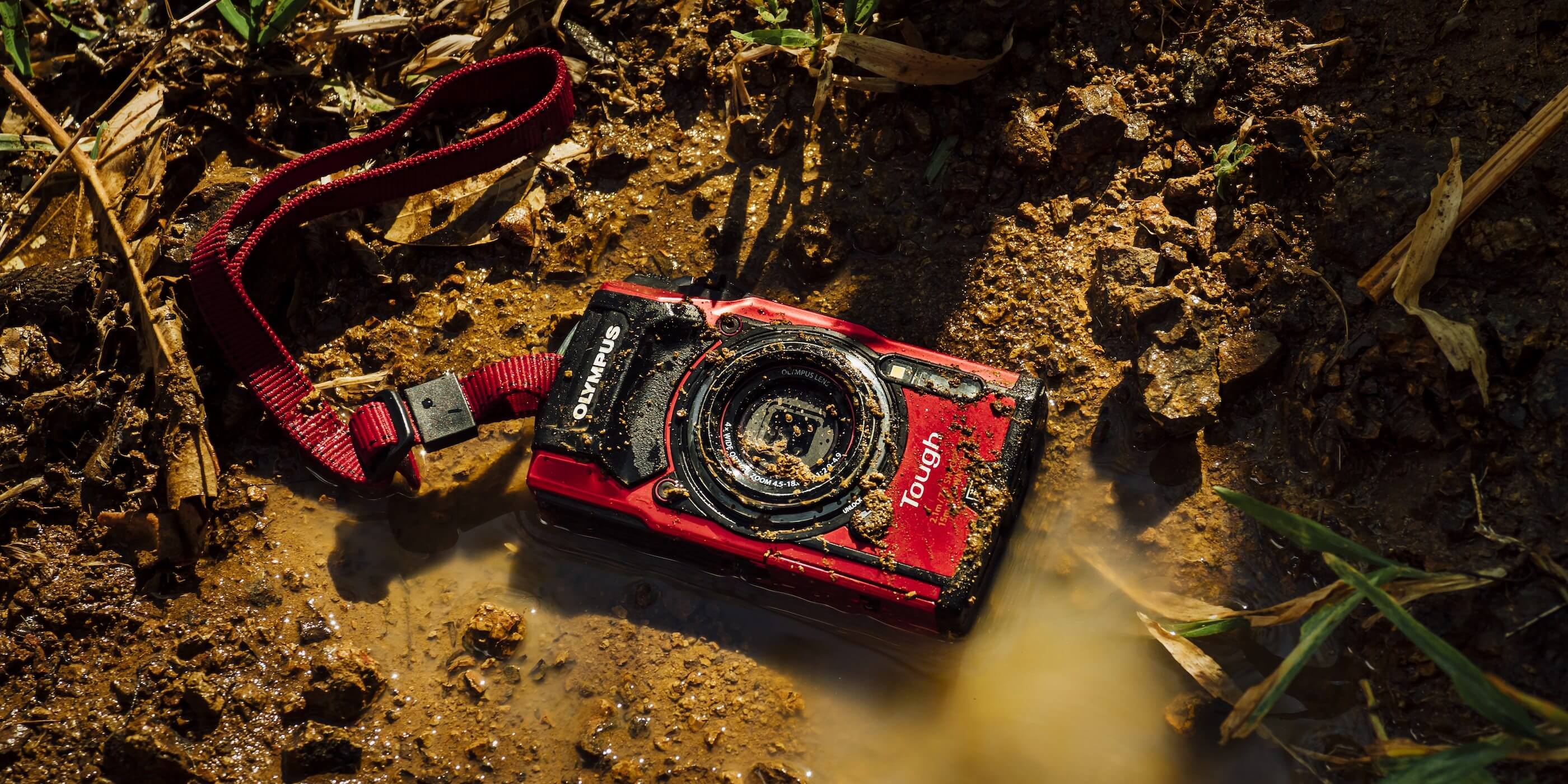 This image shows the Olympus Tough TG-5 waterproof camera on the ground in mud.