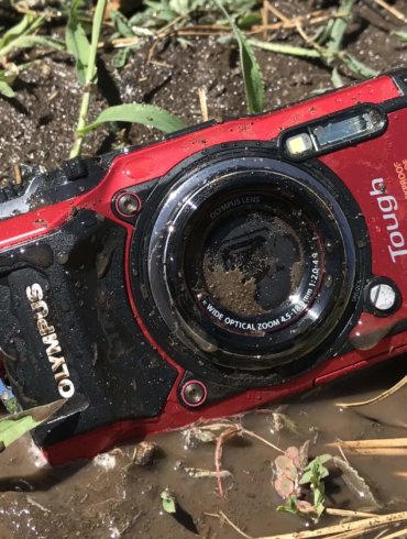 This image shows the Olympus Tough TG-5 waterproof camera in the mud on the ground.