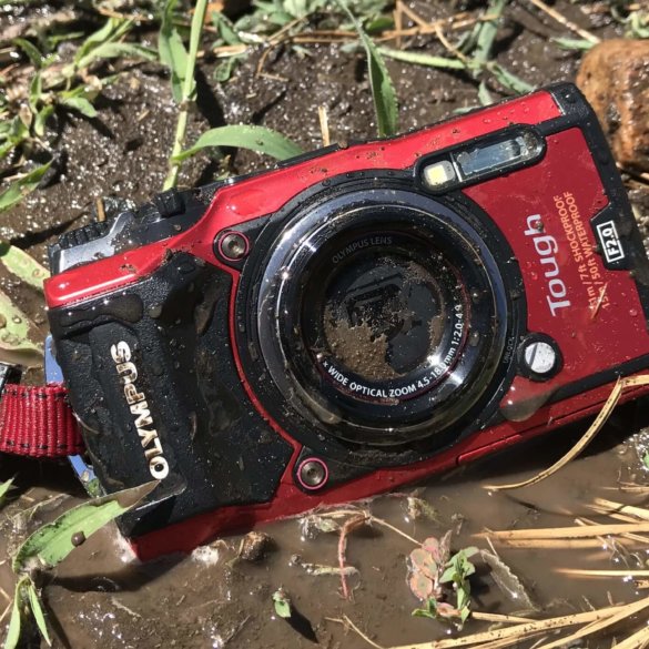 This image shows the Olympus Tough TG-5 waterproof camera in the mud on the ground.