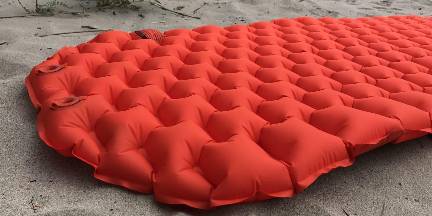This image shows the REI Co-op Flash Insulated Air Sleeping Pad in a closeup on a beach.