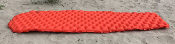 This photo shows the REI Flash Insulated Air Sleeping Pad in full length on a sandy beach.