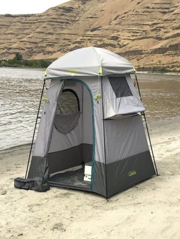 This image shows the Cabela's Privy Shelter on the bank of a river on a sandy beach.