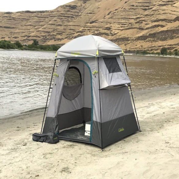 This image shows the Cabela's Privy Shelter on the bank of a river on a sandy beach.
