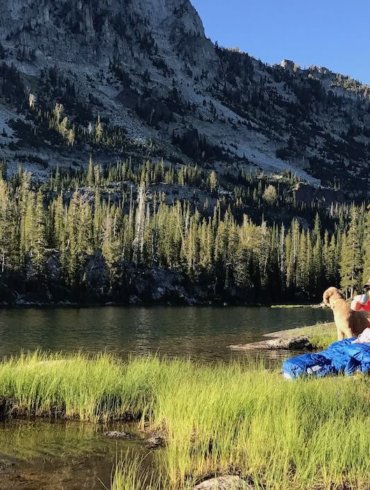 This photo shows a backpacker sitting by a mountain lake drinking coffee with the Sierra Designs Backcountry Quilt 700.