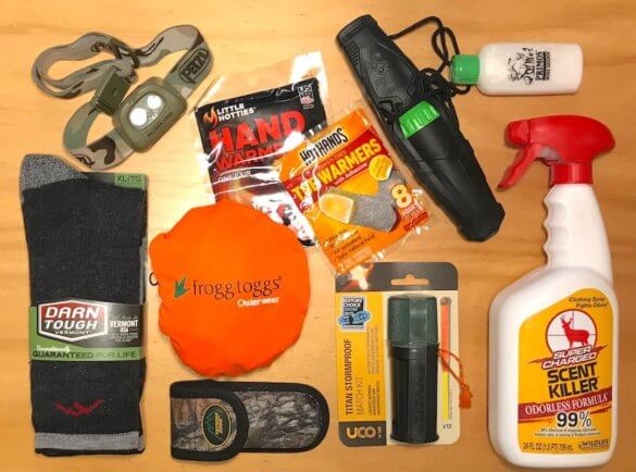 This photo shows stocking stuffers for hunters, including a deer call, wind checker, scent eliminator, wool socks, orange hunting vest, headlamp, and emergency matches.