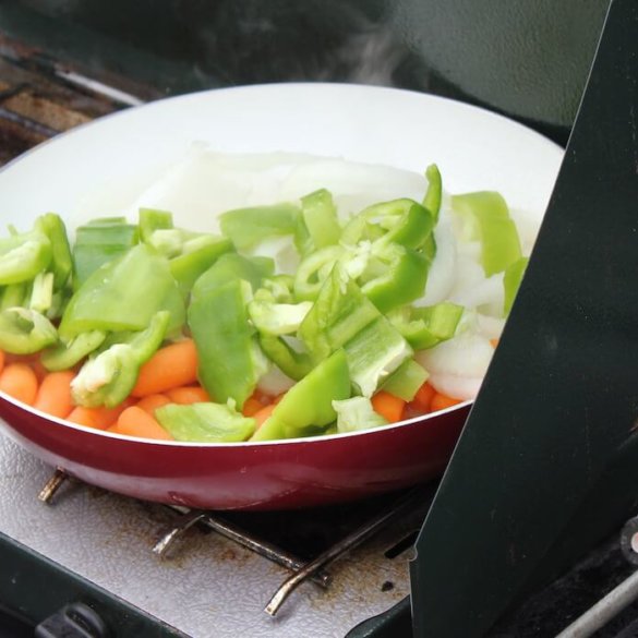 This photo shows a camp stove with a frying pan full of veggies frying outside.