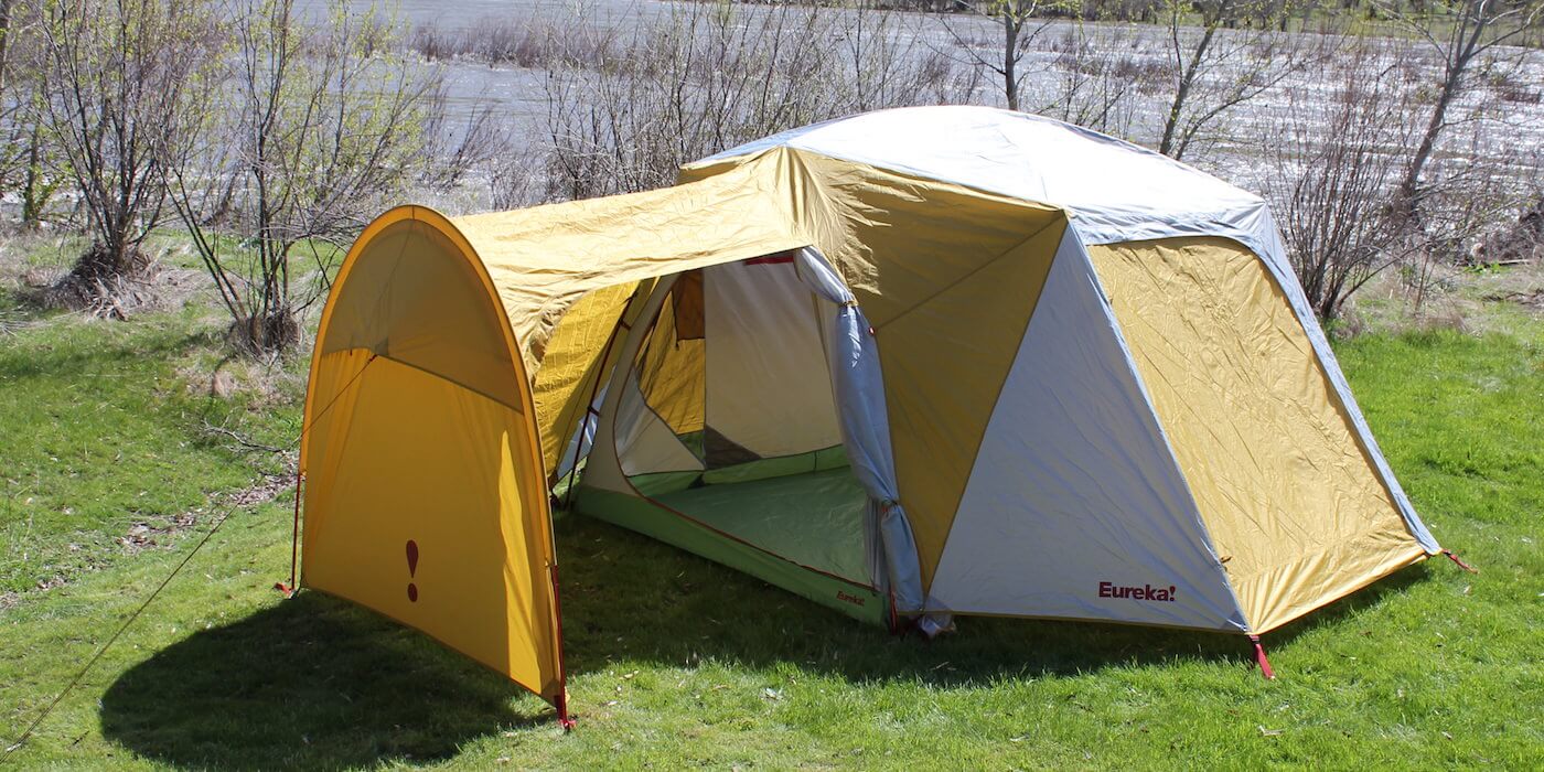 This photo shows the Eureka! Boondocker Hotel 6 Tent set up next to a river at a camping site.