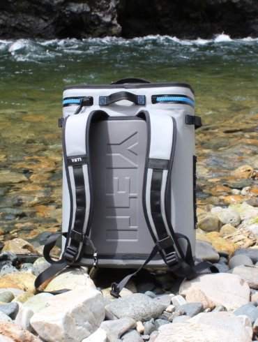 This photo shows the YETI Hopper BackFlip 24 backpack cooler on the side of a river.