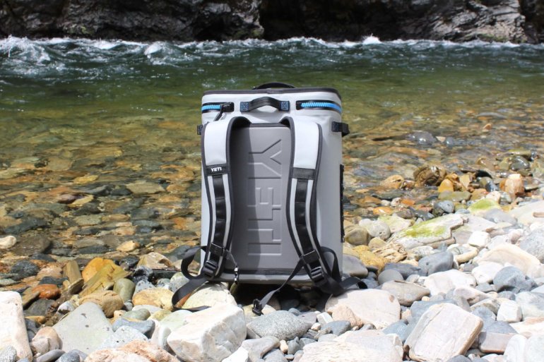 This photo shows the YETI Hopper BackFlip 24 backpack cooler on the side of a river.