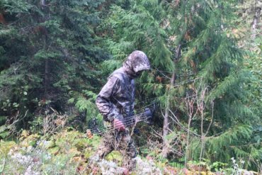 This photo shows the Cabela's Space Rain Jacket being worn by a hunter in the forest.
