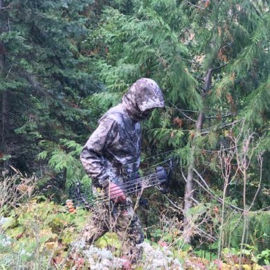 This photo shows the Cabela's Space Rain Jacket being worn by a hunter in the forest.