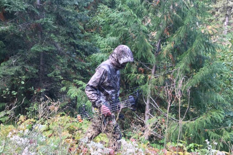 This photo shows the Cabela's Space Rain Jacket being worn by a hunter in the forest.