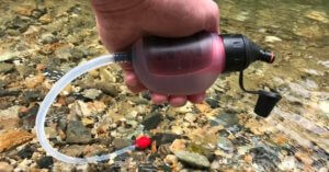 This photo shows the TrailShot portion of the MSR Trail Base Water Filter Kit held over a river.