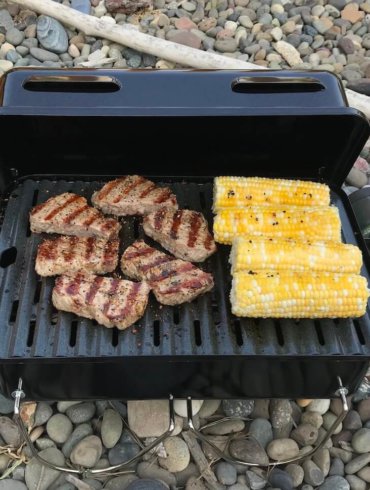 This photo shows the Weber Go-Anywhere Gas Grill with steak and corn on the cob grilling.