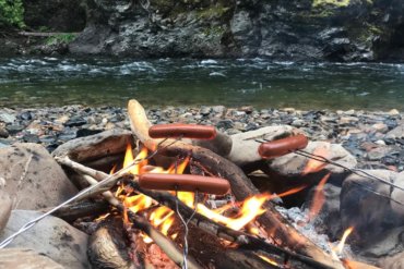 This best camping gear photo shows a campfire with hot dogs roasting over it.