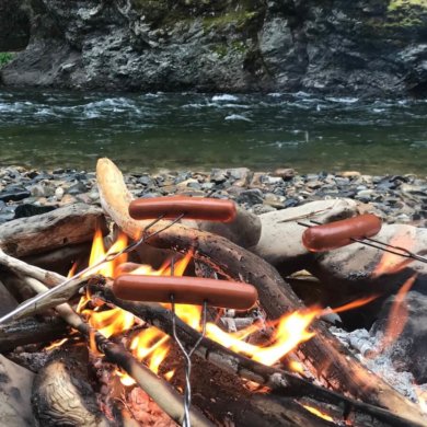 This best camping gear photo shows a campfire with hot dogs roasting over it.
