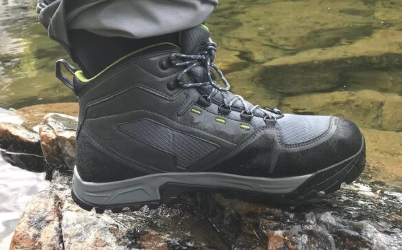 This photo shows the Orvis Ultralight Wading Boots worn with waders from a close-up side view near a river.
