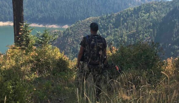 This photo shows a bowhunter standing with a hunting bow overlooking a lake.