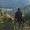 This best bowhunting gift photo shows a bowhunter standing with a hunting bow on a ridge overlooking a lake.