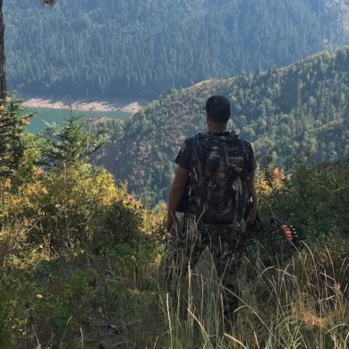 This best bowhunting gift photo shows a bowhunter standing with a hunting bow on a ridge overlooking a lake.