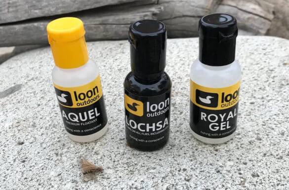 This photo shows the Loon Outdoors Aquel, Lochsa and Royal Gel fly floatant bottles on a river rock.