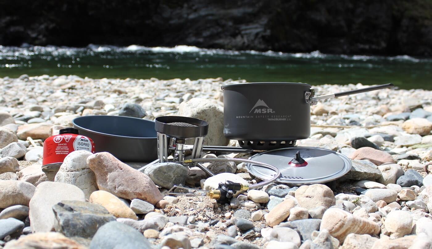 This photo shows the MSR WindBurner Stove System Combo outside near a mountain river.