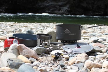 This photo shows the MSR WindBurner Stove System Combo outside near a mountain river.