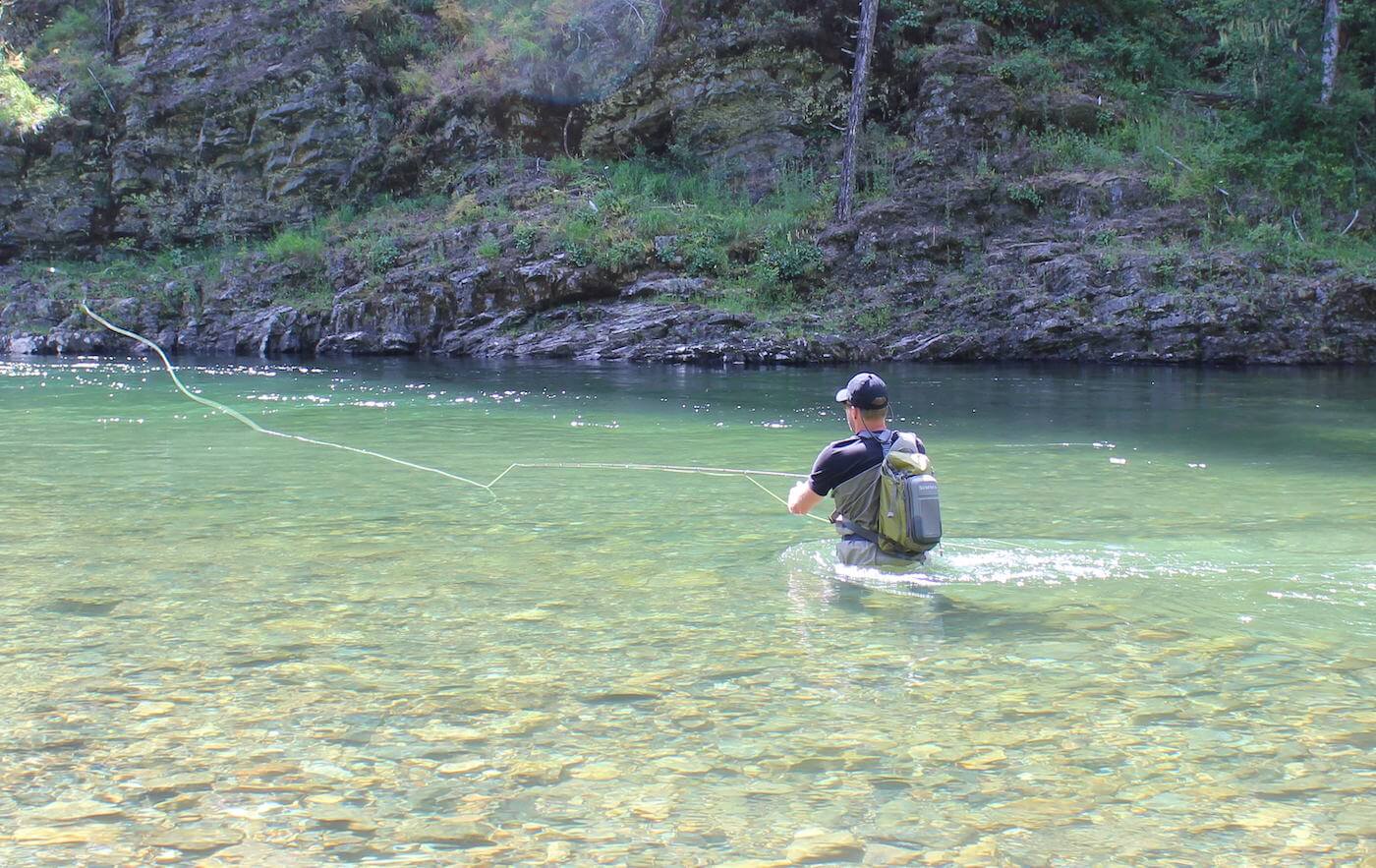 This image shows a fly fisher wading in a river while fishing with a fly rod and reel combo.