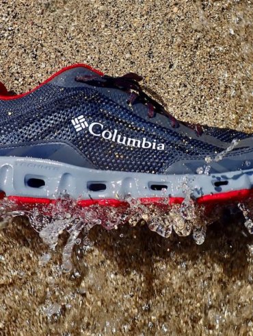 This photo shows the Columbia Drainmaker IV water shoe on beach getting hit by a small wave.