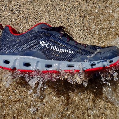 This photo shows the Columbia Drainmaker IV water shoe on beach getting hit by a small wave.