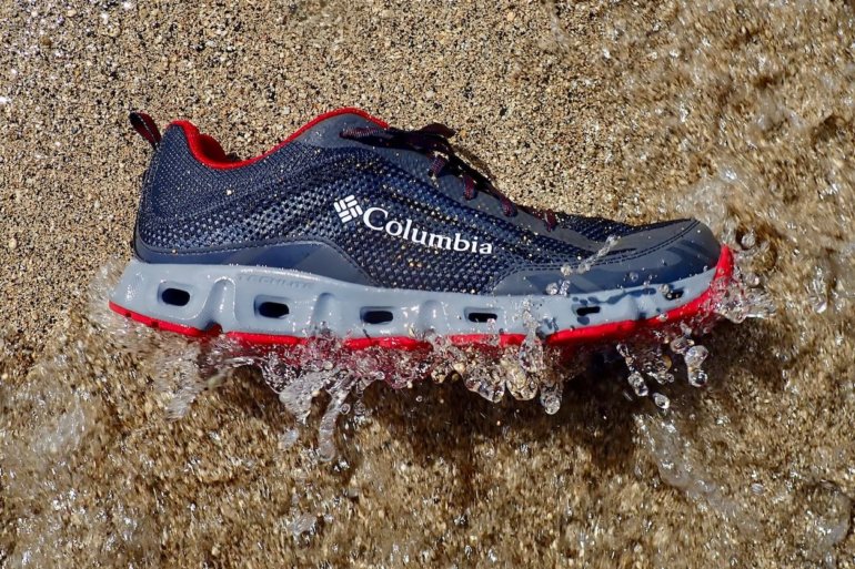 This photo shows the Columbia Drainmaker IV water shoe on beach getting hit by a small wave.