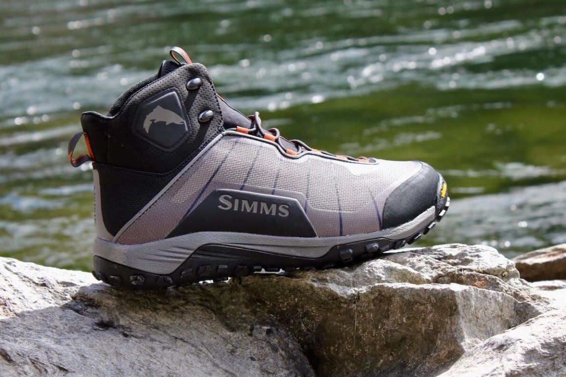 This Simms Flyweight Wading Boot Review photo shows a Simms Flyweight Wading Boot on a rock with a river in the background.