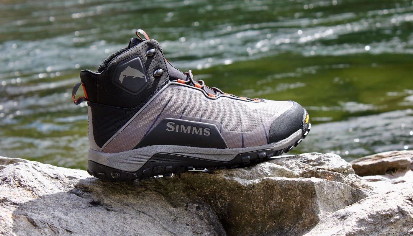 This Simms Flyweight Wading Boot Review photo shows a Simms Flyweight Wading Boot on a rock with a river in the background.