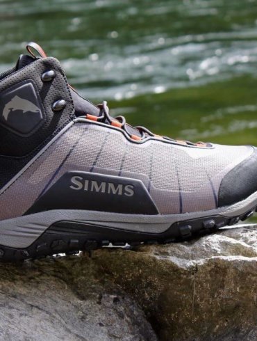 This Simms Flyweight Wading Boot Review photo shows a Simms Flyweight Wading Boot on a rock with a river in the background.