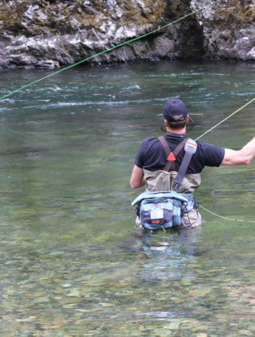 This photo shows a fly fisherman wading in a river while wearing the Umpqua Tongass 650 Waterproof Waist Pack.
