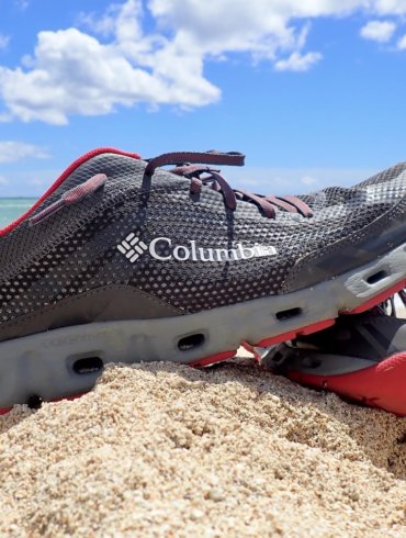 This photo shows a pair of water shoes on a sandy beach near the ocean.