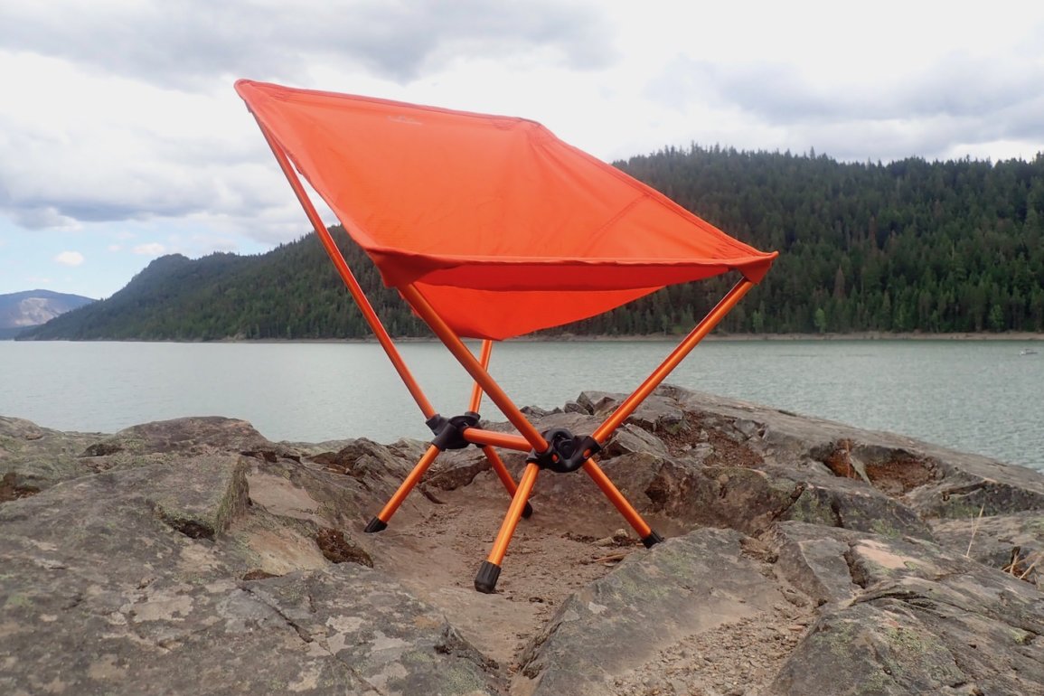 This gear review photo shows the REI Co-op Flexlite Air Chair on a rock above a lake.