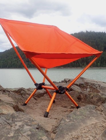This gear review photo shows the REI Co-op Flexlite Air Chair on a rock above a lake.