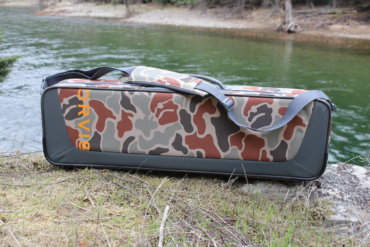 This review photo shows the Orvis Safe Passage Carry It All fly fishing travel bag case outside near a river.