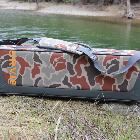 This review photo shows the Orvis Safe Passage Carry It All fly fishing travel bag case outside near a river.
