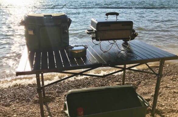 This photo shows the Mountain Summit Gear Heavy-Duty Roll-Top X-Large Table set up outside near a lake.