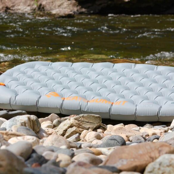 Sea to Summit Ether Light XT Insulated Air Mat inflated on a rocky shoreline near a mountain river.