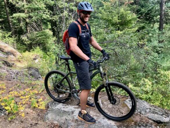 This photo shows the author with the REI Co-op Cycles DRT 1.2 mountain bike outside on a mountain trail. 