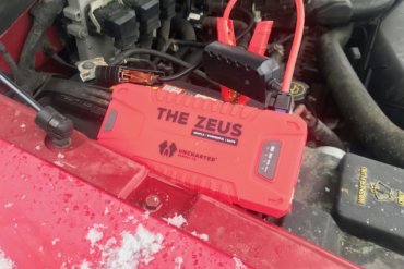 This photo shows the Uncharted Supply Co 'The Zeus' portable jump starter attached to a dead auto battery.