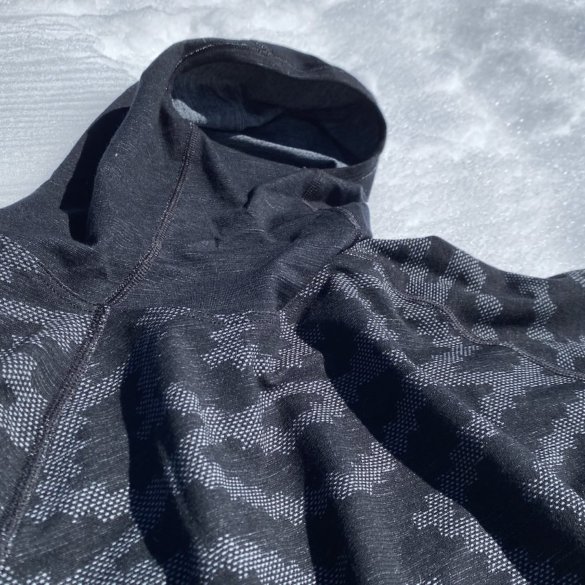 This photo shows the Odlo Natural + Kinship Warm Base Layer Top with Face Mask outside on snow.