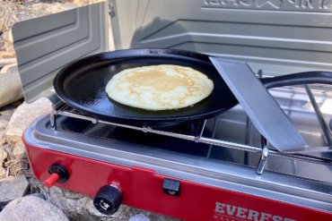 This best camping stoves photo shows a camping stove with a cooking pancake outside.