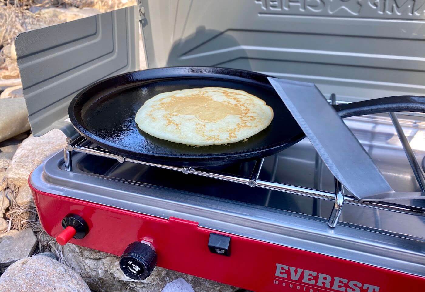 This best camping stoves photo shows a camping stove with a cooking pancake outside.